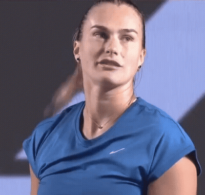 A Woman In A Blue Shirt And Necklace Is Looking At The Camera . GIF