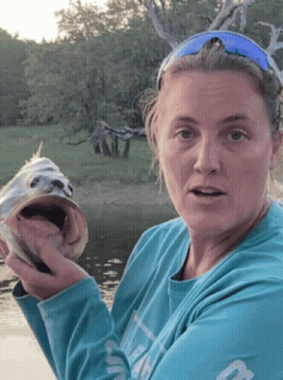 A Woman In A Blue Shirt Is Holding A Fish GIF
