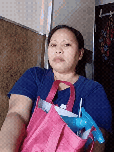 A Woman In A Blue Shirt Is Holding A Pink Bag With A Spray Bottle In It GIF
