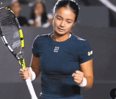 A Woman In A Blue Shirt Is Holding A Tennis Racquet In Her Hands GIF