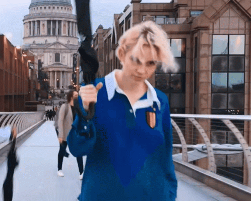 A Woman In A Blue Shirt Is Holding An Umbrella Over Her Shoulder GIF