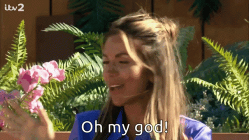 A Woman In A Blue Shirt Is Holding Flowers And Saying Oh My God GIF