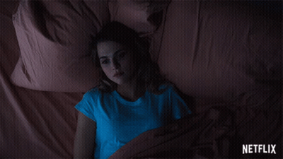 A Woman In A Blue Shirt Is Laying On A Bed With A Netflix Logo In The Corner GIF