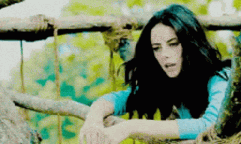 A Woman In A Blue Shirt Is Leaning On A Tree Branch GIF