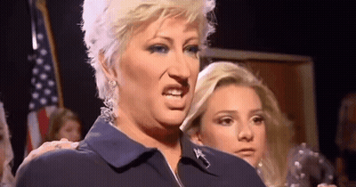 A Woman In A Blue Shirt Is Making A Funny Face In Front Of A Group Of People . GIF