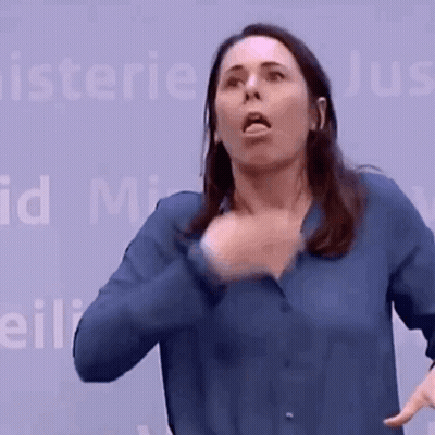 A Woman In A Blue Shirt Is Making A Funny Face In Front Of A Sign That Says Minister GIF