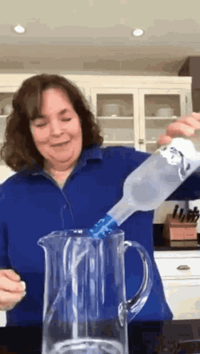 A Woman In A Blue Shirt Is Pouring A Bottle Of Water Into A Pitcher . GIF
