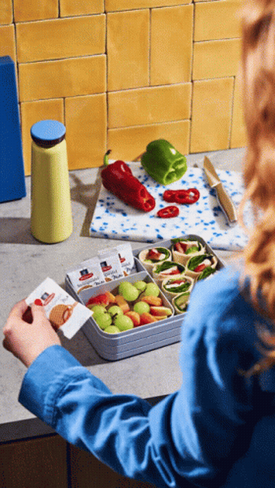 A Woman In A Blue Shirt Is Putting A Sandwich In A Container With Fruit GIF