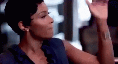 A Woman In A Blue Shirt Is Sitting At A Table With Her Hand Up . GIF