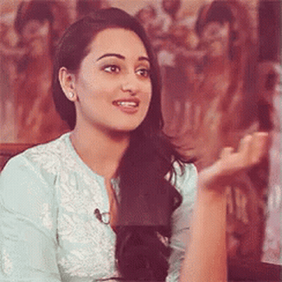 A Woman In A Blue Shirt Is Sitting In Front Of A Painting And Talking To Someone . GIF