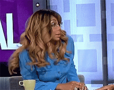 A Woman In A Blue Shirt Is Sitting In Front Of A Purple Wall With The Letter L On It GIF