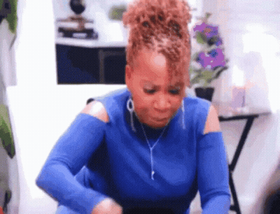 A Woman In A Blue Shirt Is Sitting On A Couch And Looking At Her Phone . GIF
