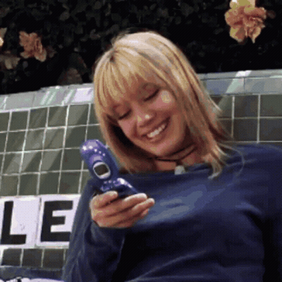 A Woman In A Blue Shirt Is Smiling While Holding A Purple Cell Phone GIF