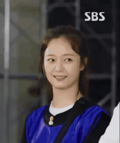 A Woman In A Blue Shirt Is Smiling With The Sbs Logo Behind Her GIF