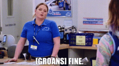 A Woman In A Blue Shirt Is Standing At A Counter In A Store And Talking To A Customer . GIF