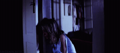 A Woman In A Blue Shirt Is Standing In A Doorway With The Words " Undead Critic " On The Bottom Right GIF