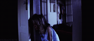 A Woman In A Blue Shirt Is Standing In A Doorway With The Words Undeadcritic On The Bottom Right GIF