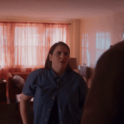A Woman In A Blue Shirt Is Standing In A Room GIF