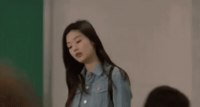 A Woman In A Blue Shirt Is Standing In Front Of A Green Wall . GIF