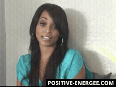 A Woman In A Blue Shirt Is Standing In Front Of A White Wall With A Positive-Energiee.com Logo GIF