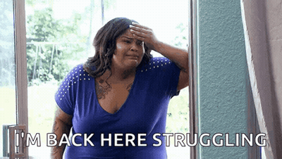 A Woman In A Blue Shirt Is Standing In Front Of A Window And Covering Her Forehead With Her Hand . GIF