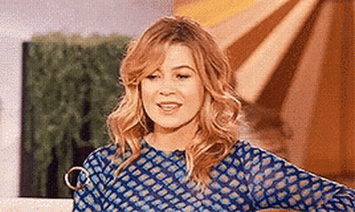A Woman In A Blue Shirt Is Standing In Front Of A Window . GIF