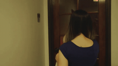 A Woman In A Blue Shirt Is Walking Through A Doorway GIF