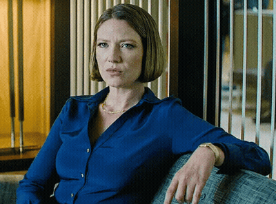 A Woman In A Blue Shirt Sits On A Grey Couch GIF