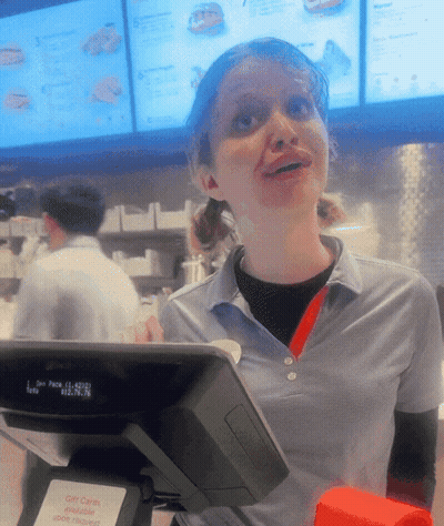 A Woman In A Blue Shirt Stands Behind A Cash Register That Says Gift Cards GIF