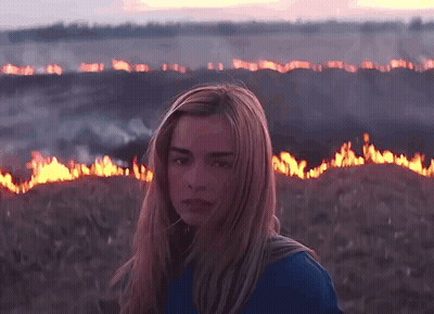 A Woman In A Blue Shirt Stands In Front Of A Field Of Fire GIF