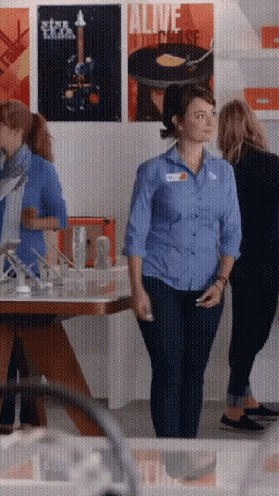 A Woman In A Blue Shirt Stands In Front Of A Poster That Says " Alive In The Chase " GIF
