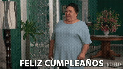 A Woman In A Blue Shirt Stands In Front Of A Sign That Says " Feliz Cumpleanos " GIF