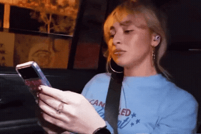 A Woman In A Blue Shirt That Says Canceled Is Looking At Her Phone GIF