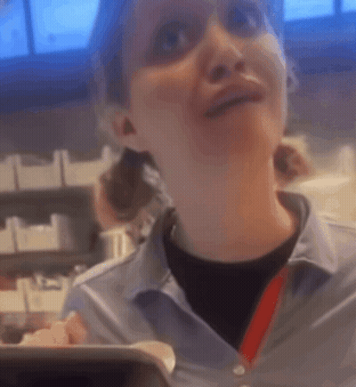 A Woman In A Blue Shirt With A Red Lanyard Around Her Neck Is Smiling GIF