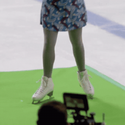 A Woman In A Blue Skirt Is Standing On A Green Mat Wearing Ice Skates GIF