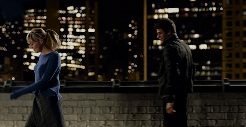 A Woman In A Blue Sweater Is Being Held By A Man In A Black Suit GIF