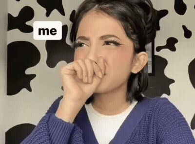 A Woman In A Blue Sweater Is Covering Her Mouth With Her Hand In Front Of A Cow Print Wall . GIF