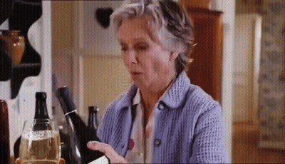 A Woman In A Blue Sweater Is Holding A Bottle Of Wine And A Glass Of Wine . GIF