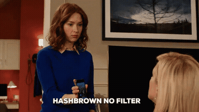 A Woman In A Blue Sweater Is Holding A Cell Phone With The Words Hashbrown No Filter Below Her GIF