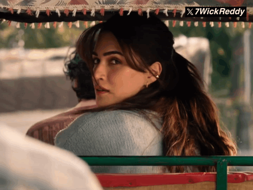 A Woman In A Blue Sweater Is Looking Over Her Shoulder With A X7wick Reddy Logo In The Corner GIF