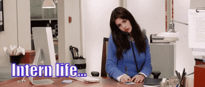 A Woman In A Blue Sweater Is Sitting At A Desk In Front Of A Computer With The Words Intern Life Written Above Her GIF