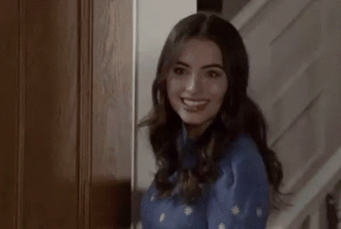 A Woman In A Blue Sweater Is Standing In A Doorway Looking At The Camera . GIF