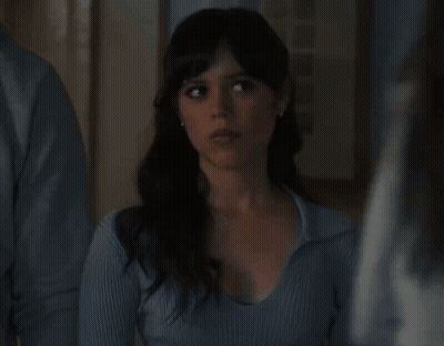 A Woman In A Blue Sweater Is Standing Next To A Man And Looking At The Camera . GIF