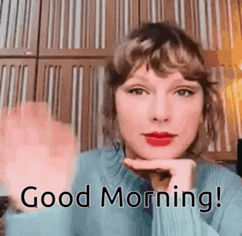 A Woman In A Blue Sweater Is Waving Her Hand And Says Good Morning . GIF