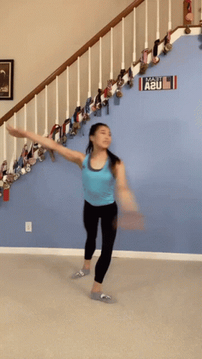 A Woman In A Blue Tank Top Is Dancing In Front Of A Sign That Says A2u GIF