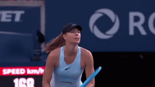 A Woman In A Blue Tank Top Is Holding A Tennis Racquet On A Court . GIF