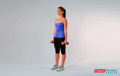 A Woman In A Blue Tank Top Is Holding Dumbbells Over Her Shoulder GIF