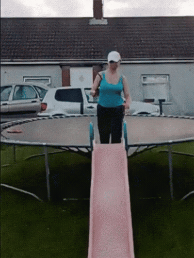 A Woman In A Blue Tank Top Is On A Pink Slide On A Trampoline GIF