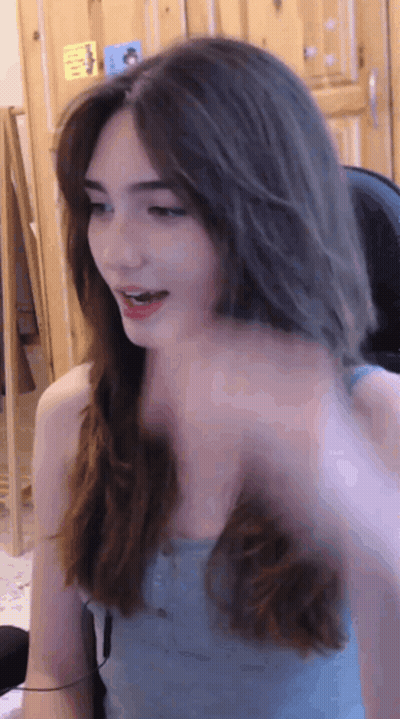 A Woman In A Blue Tank Top Is Sitting In Front Of A Wooden Door GIF