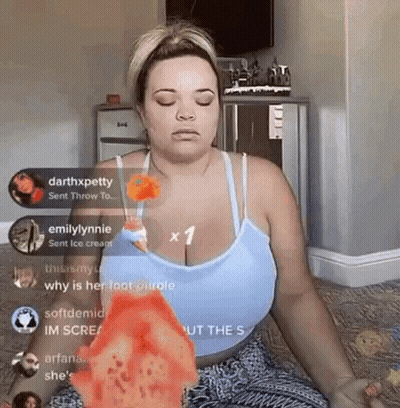 A Woman In A Blue Tank Top Is Sitting On The Floor With Her Eyes Closed And Holding A Slice Of Pizza . GIF